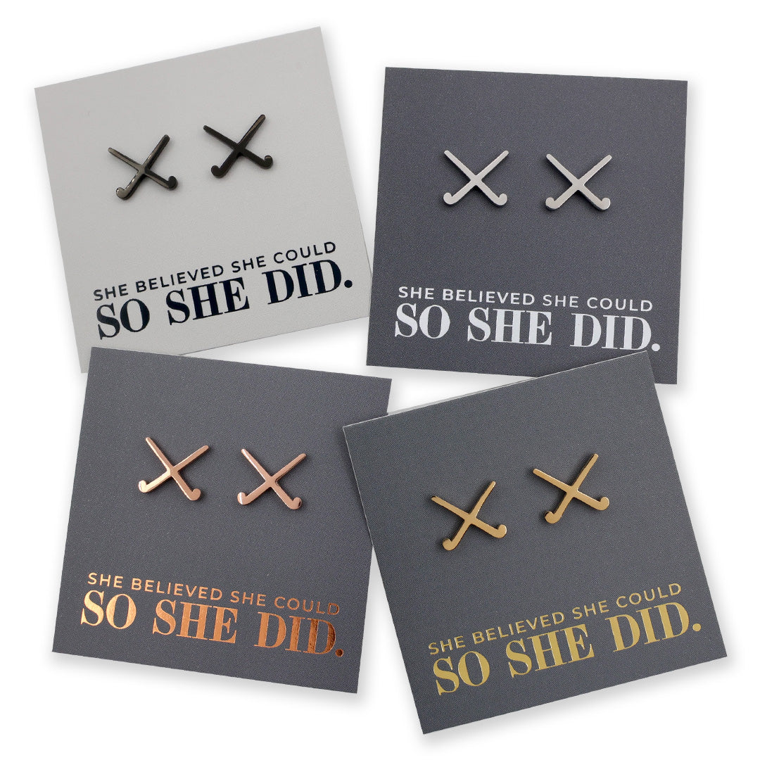 Four pairs of field hockey earrings on grey cards with 'She believed she could so she did' text.