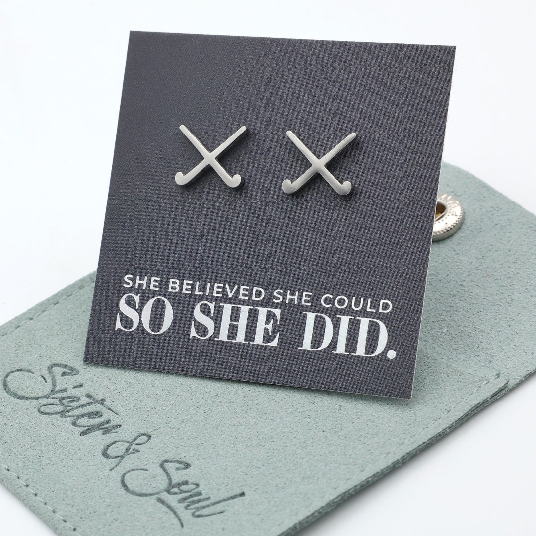 Silver stainless steel hockey earrings on a card with 'She believed she could so she did' text, displayed on a branded card.