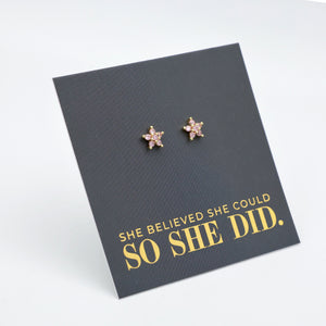 Pink cubic zirconia star shaped studs presented on a grey card with gold 'She Believed She Could So She Did' writing.