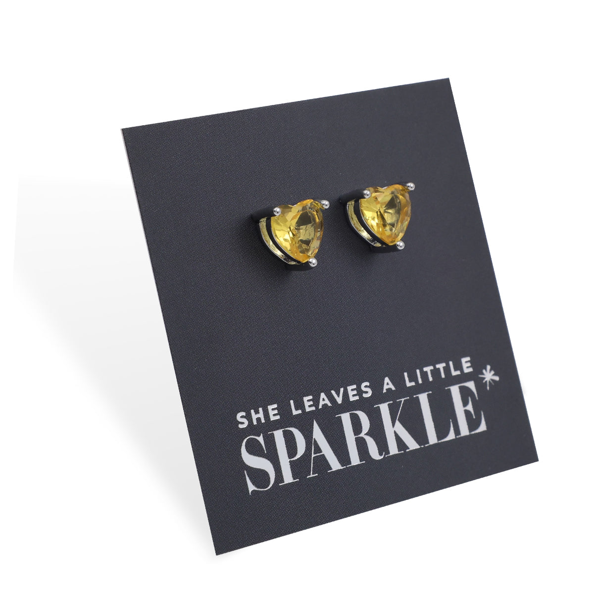 Heart-shaped yellow gemstone earrings on a black card with 'She Leaves a Little Sparkle' text.