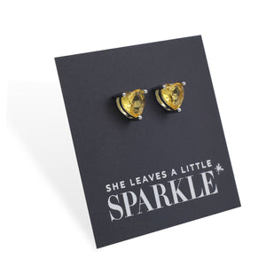 Heart-shaped yellow gemstone earrings on a black card with 'She Leaves a Little Sparkle' text.
