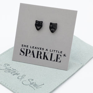 Black mask earrings on a card with 'She leaves a little sparkle' text, displayed on a light gray surface.