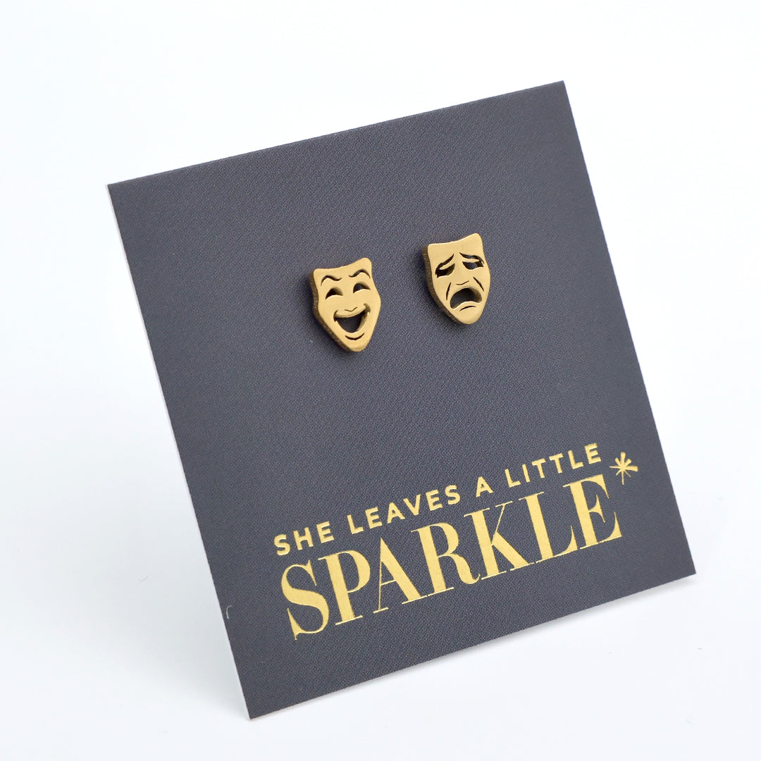 Gold theater mask earrings on a dark gray card with 'She Leaves a Little Sparkle' text.
