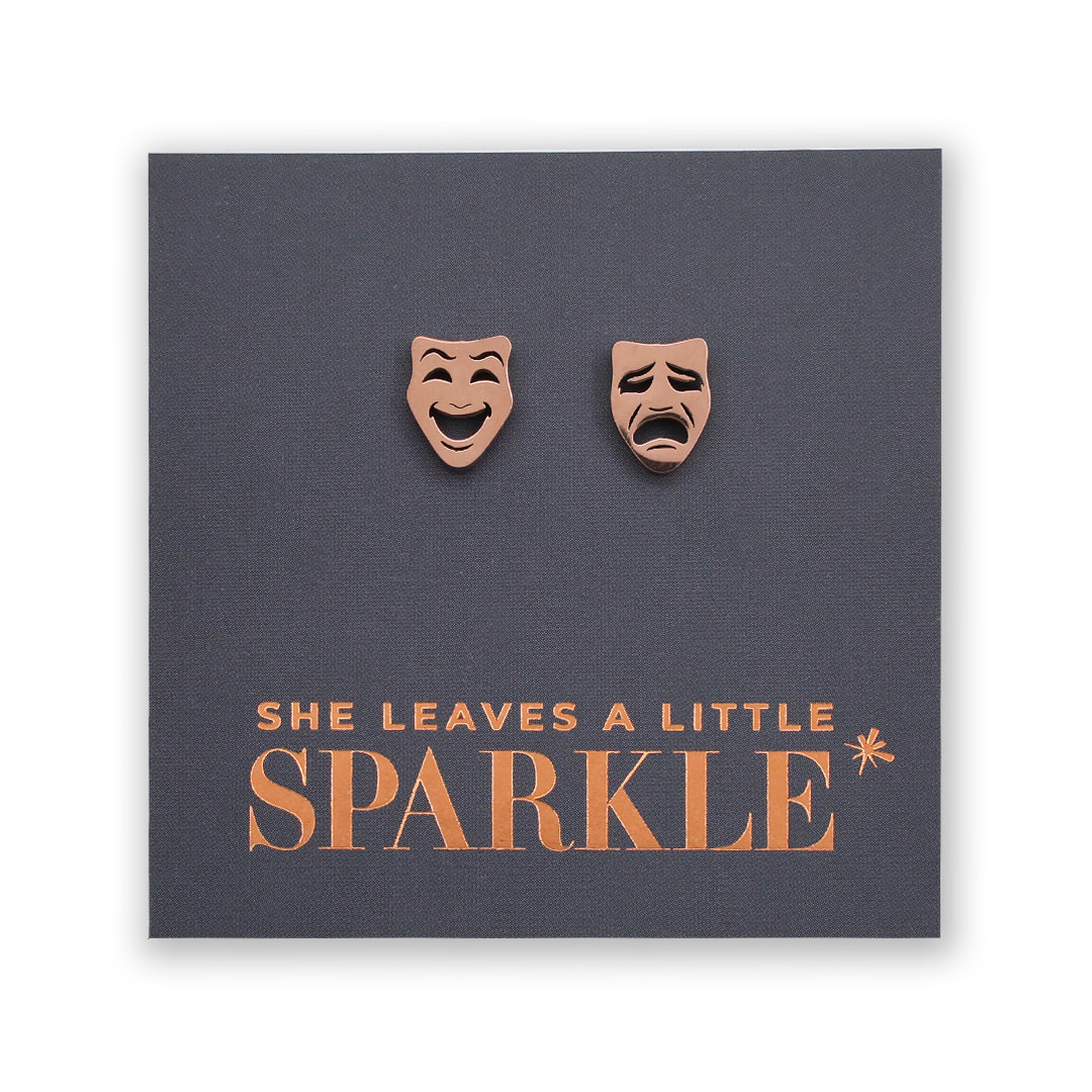Earrings shaped like comedy and tragedy masks on a card with 'She Leaves a Little Sparkle' text.