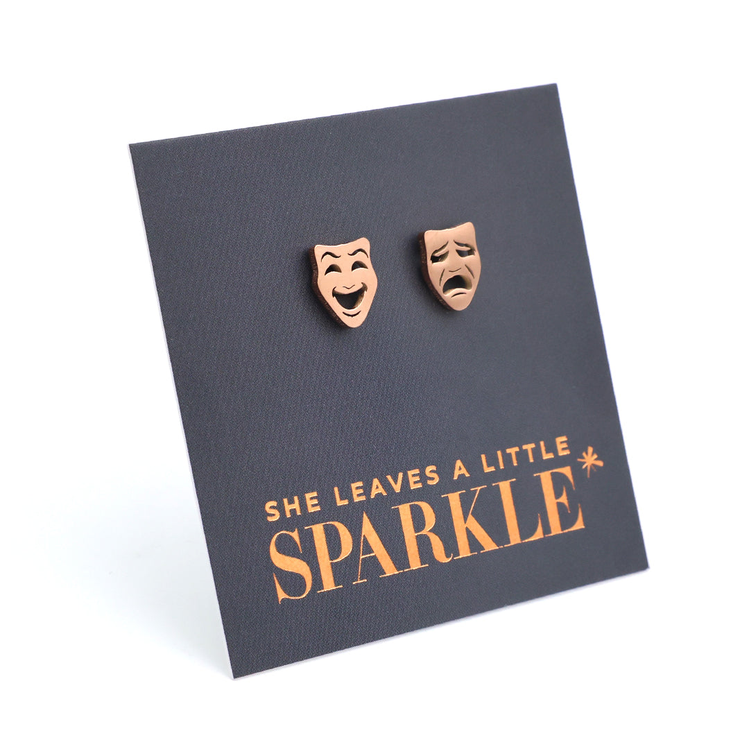 Pair of earrings shaped like comedy and tragedy masks on a 'She Leaves a Little Sparkle' card.