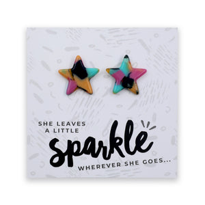 Two star-shaped stud earrings with a colorful marbled pattern in pink, blue, yellow, and black, displayed on a white printed card with the text 'SHE LEAVES A LITTLE sparkle WHEREVER SHE GOES.
