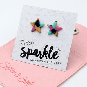 Two star-shaped stud earrings with a multicolor tie-dye pattern of pink, yellow, blue, and black, displayed on a white card that reads 'sparkle' with the Sister & Soul brand logo on a pink pouch.