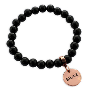 Black beaded bracelet with a rose gold 'BRAVE' charm on a white background