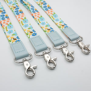 Sky Blue Floral lanyards showing Be Kind, Teach Love Inspire, You Got This and So Loved embossed trims and lobster clasps.