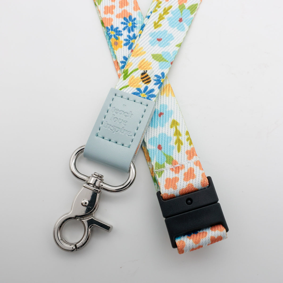 Teach Love Inspire embossed on a colourful floral lanyard with pale blue trim and a lobster clasp.