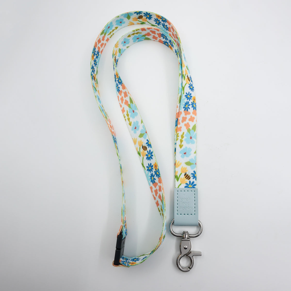 Teach Love Inspire embossed on a colourful floral lanyard with pale blue trim and a lobster clasp.