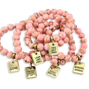 Pink beaded bracelet with gold charm tags on a white background