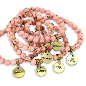 Pink beaded bracelets with gold charms and engraved words on a white background