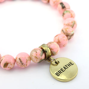 Pink beaded bracelet with a gold 'BREATHE' tag on a white background