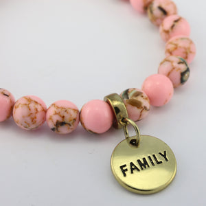 Pink beaded bracelet with a gold 'FAMILY' charm on a light gray background