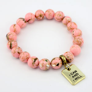 Pink beaded bracelet with a gold 'I Can and I Will' charm on a white background