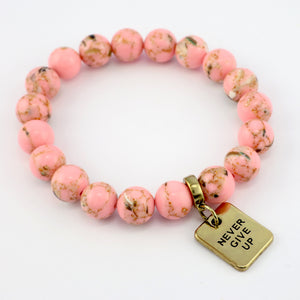Pink beaded bracelet with a gold 'Never Give Up' tag on a white background