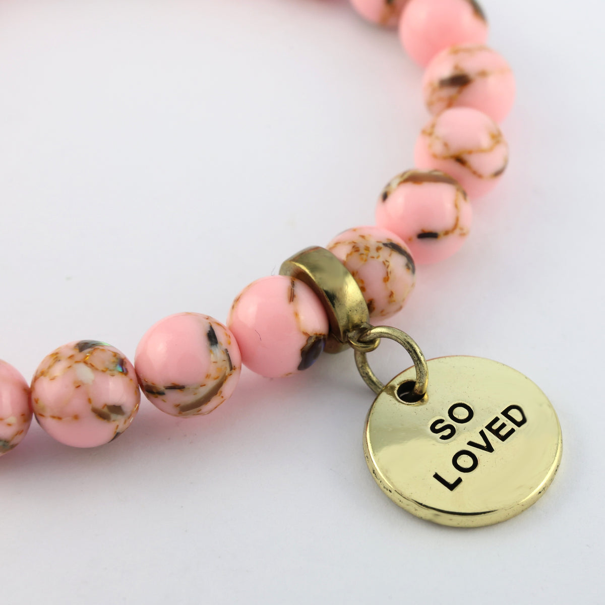 Pink beaded bracelet with a gold 'SO LOVED' charm on a light background