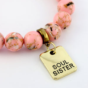 Bracelet with pink beads and a gold 'Soul Sister' charm on a white background