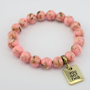 Pink beaded bracelet with a gold tag saying 'You Got This' on a light gray background