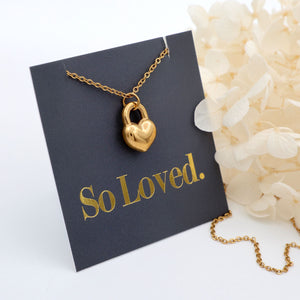 Gold heart-shaped padlock necklace on a 'So Loved' card with flowers in the background