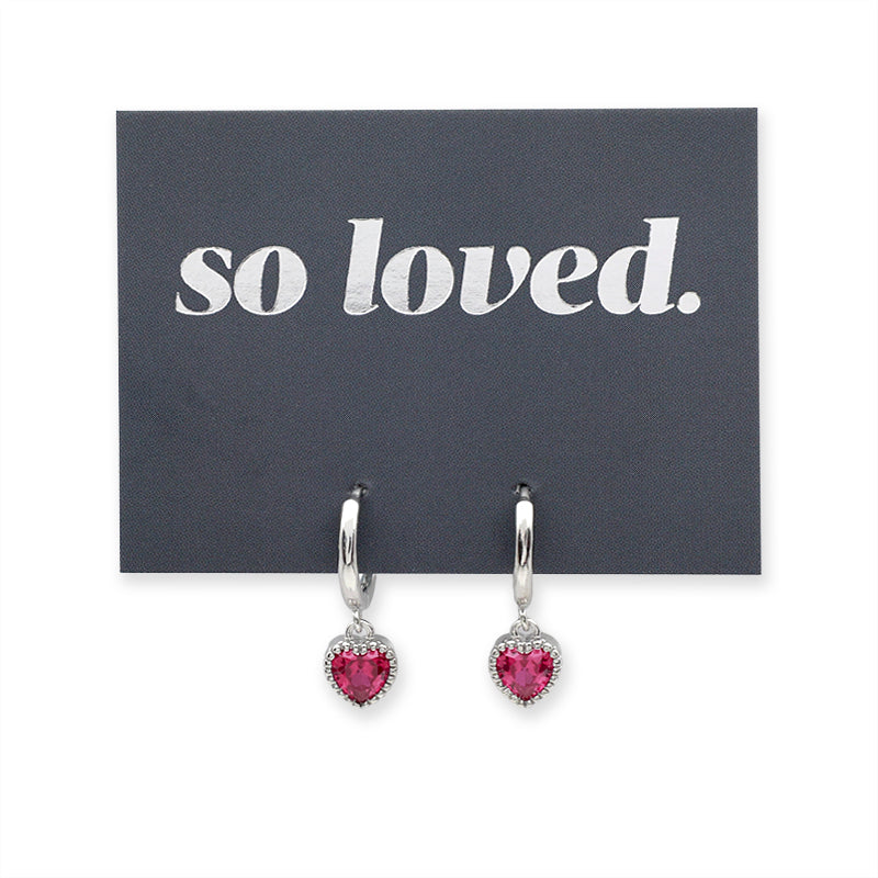 Pink heart shaped huggies dangle earrings presented on a grey card with silver 'so loved' writing.