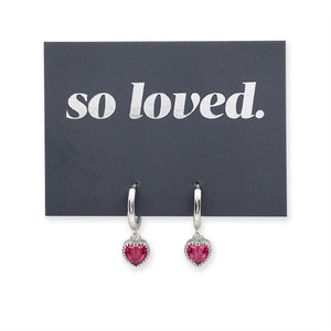 Pink heart shaped huggies dangle earrings presented on a grey card with silver 'so loved' writing.