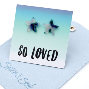 Star-shaped stud earrings with a blue and white marbled pattern, displayed on a white card that reads 'SO LOVED' with a light blue fabric pouch underneath. The brand 'Sister & Soul' is visible on the pouch.