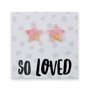 A pair of star-shaped stud earrings in a soft pink and pale yellow gradient, displayed on a white card with gray polka dots and the text 'SO LOVED' in black.