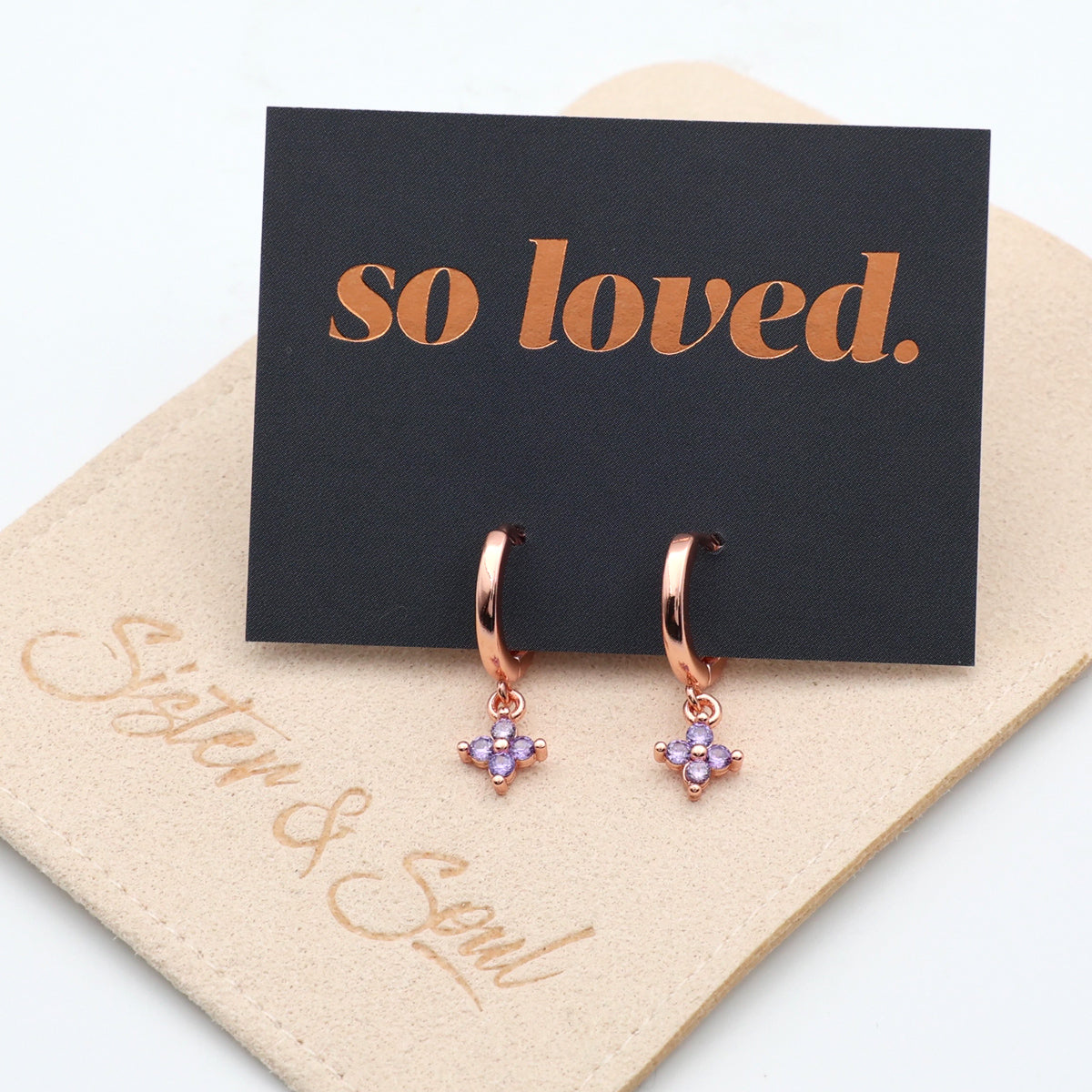 Rose gold hoop earrings with purple stones on a 'so loved' card with beige backing