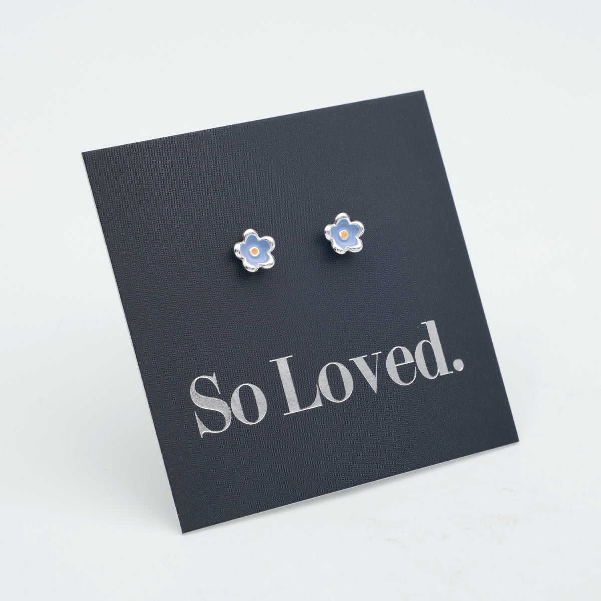 Blue flower earrings with blue and orange enamel detail on a grey card with silver 'So Loved' writing. 