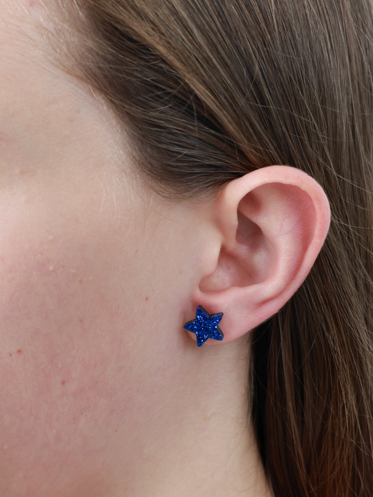 She Leaves A Little Sparkle star acrylic glitter stud earrings in dark blue glitter worn on an ear to show size and fit