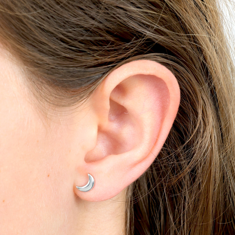 Close-up of an ear wearing a silver moon-shaped earring with hair partially covering the frame.