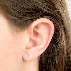 Close-up of an ear wearing a silver moon-shaped earring with hair partially covering the frame.