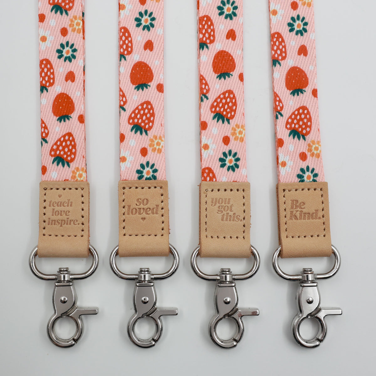 Strawberry Patch lanyards showing Be Kind, Teach Love Inspire, You Got This and So Loved embossed trims and lobster clasps.