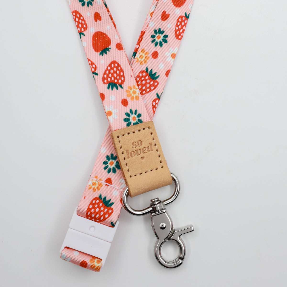 So Loved embossed on a pink strawberry and flower lanyard with tan trim and a lobster clasp.