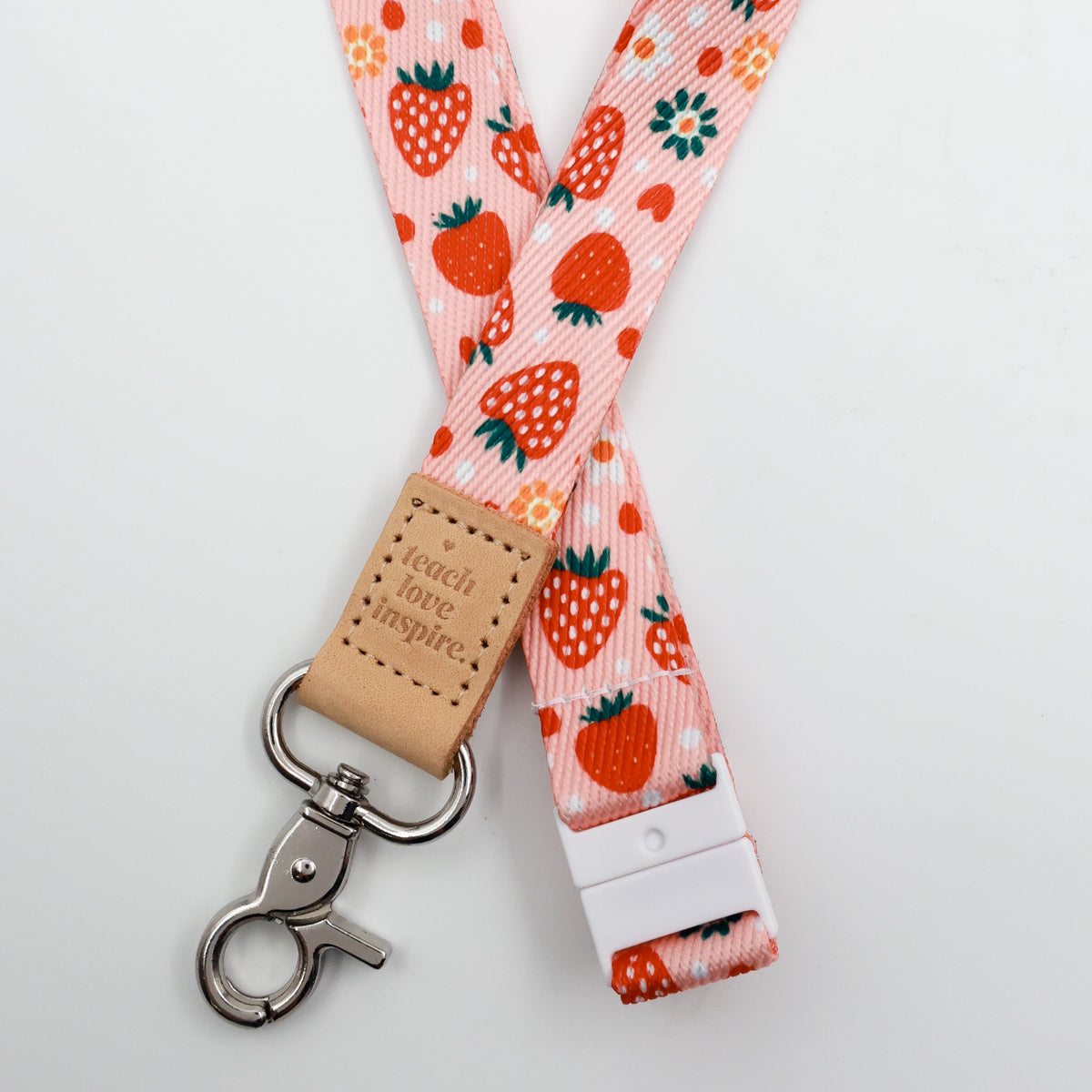 Teach Love Inspire embossed on a pink strawberry and flower lanyard with tan trim and a lobster clasp.