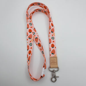 Teach Love Inspire embossed on a pink strawberry and flower lanyard with tan trim and a lobster clasp.