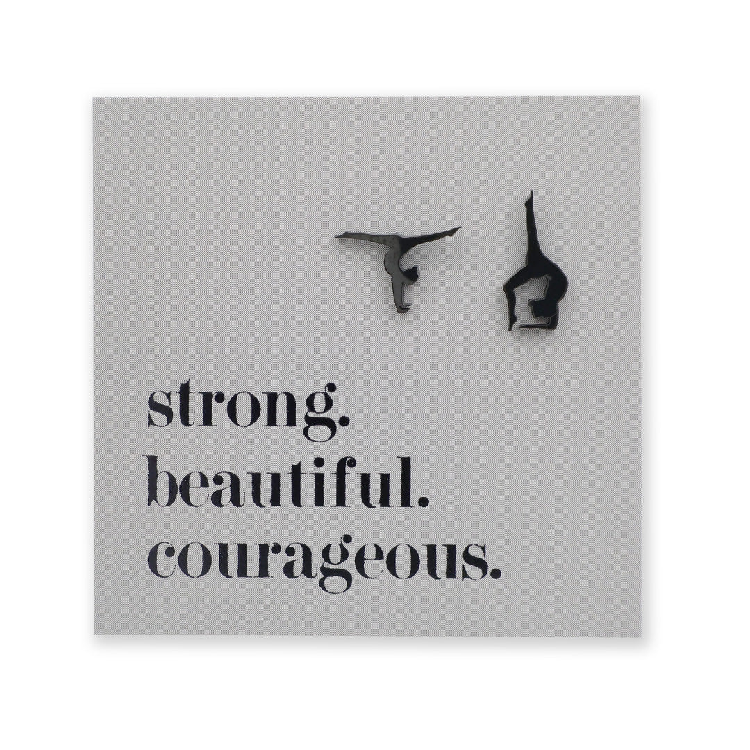 Black stainless steel gymnastics figure shaped earrings on a grey card with 'strong. beautiful. courageous.' text