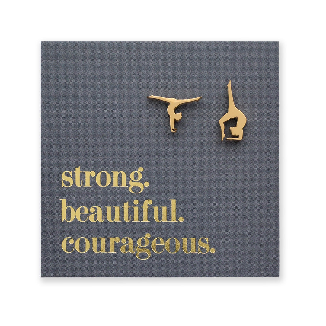 Gold gymnastics pose earrings on a dark gray card with 'strong. beautiful. courageous.' text.