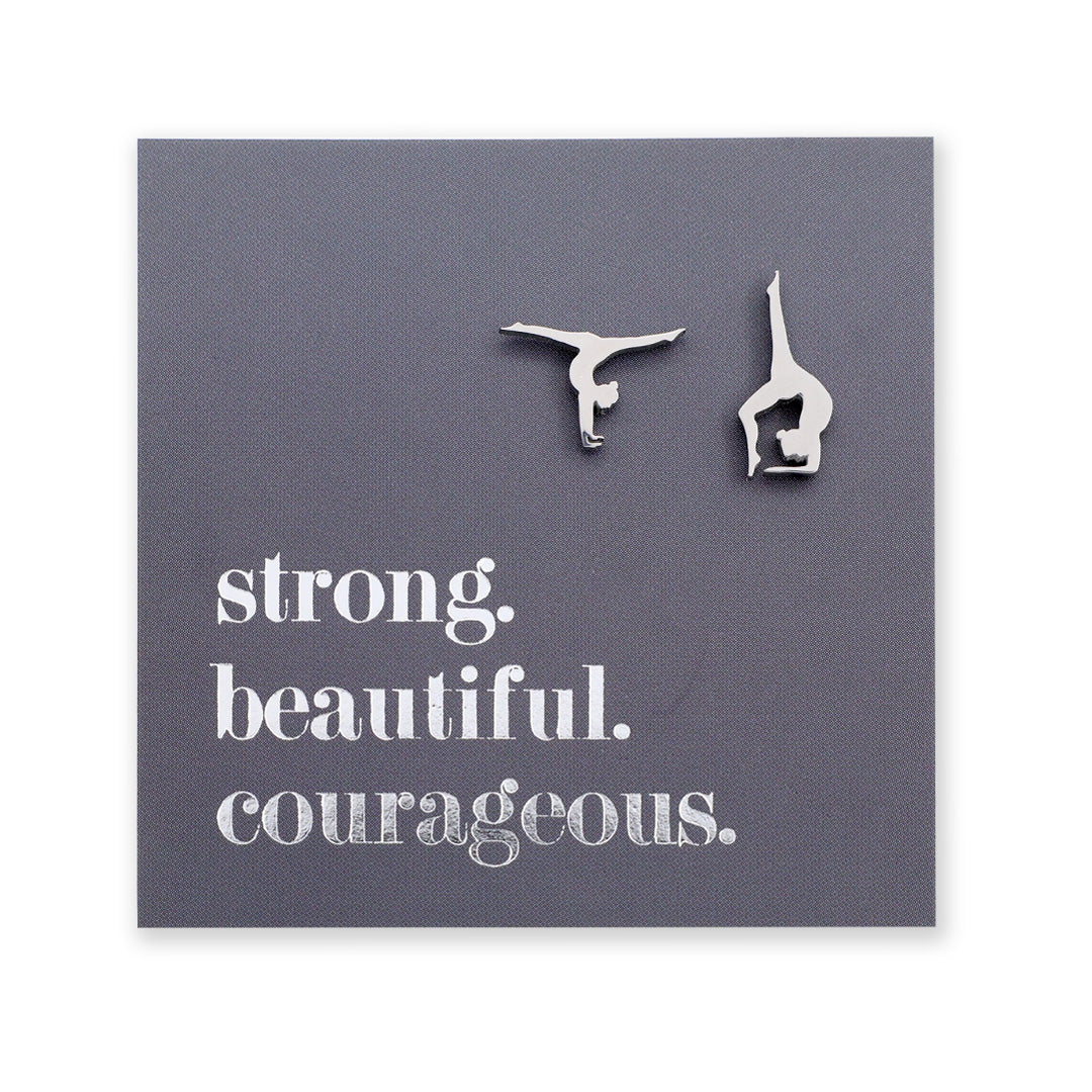 Silver hypoallergenic stainless steel gymnastics figure shaped earrings on a grey card with 'strong. beautiful. courageous.' text