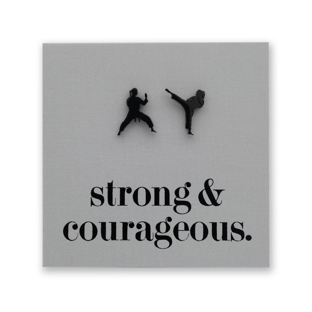A square gray wall art print featuring two black silhouettes of martial artists in action above the phrase 'strong & courageous.' in black serif text, shown against a white background.