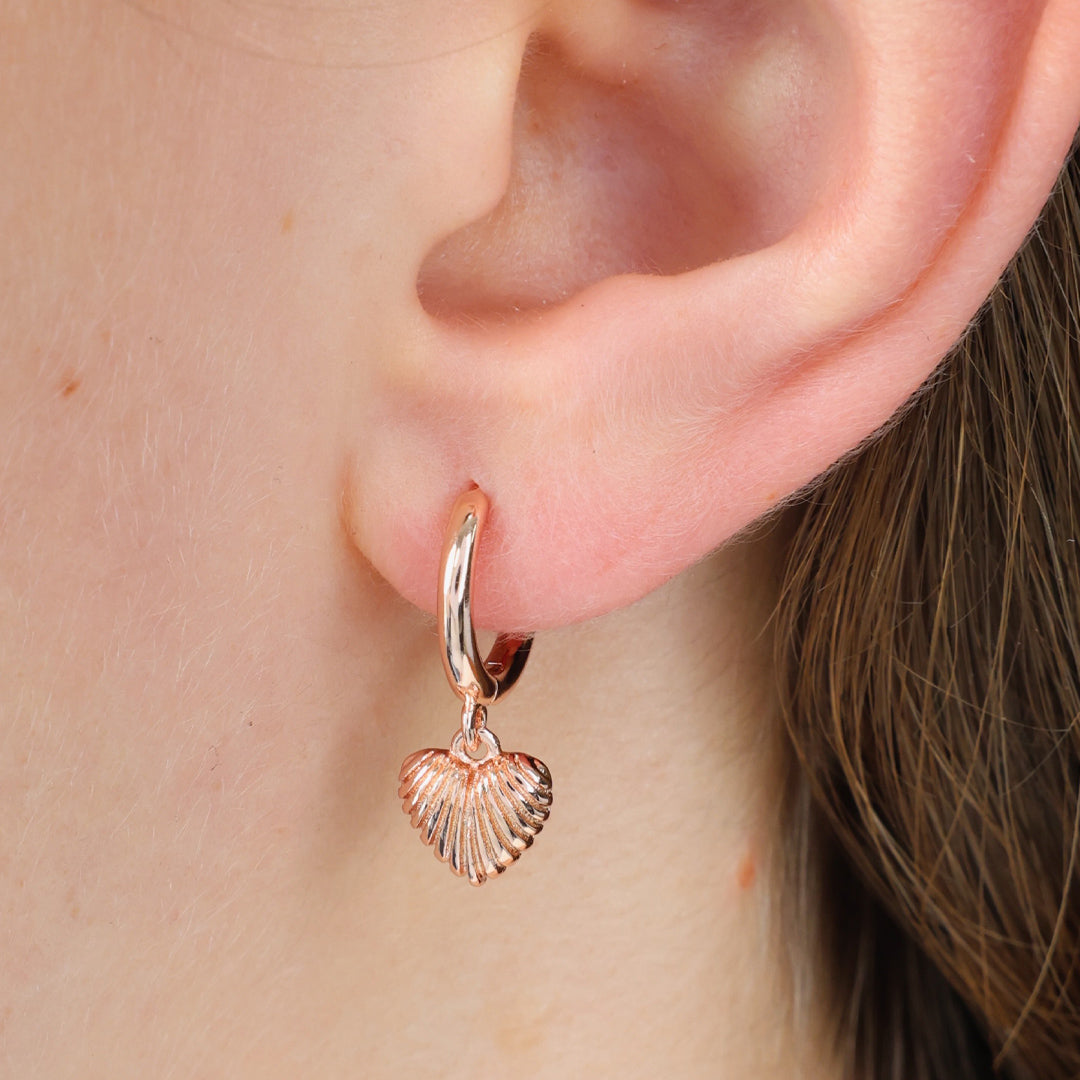 Rose gold heart earrings shown in a girls ear. 