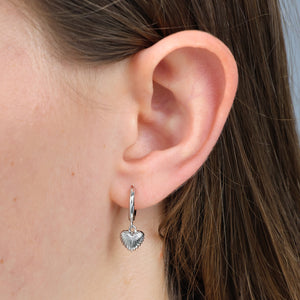 Close-up of an ear wearing a silver heart-shaped earring with blurred background