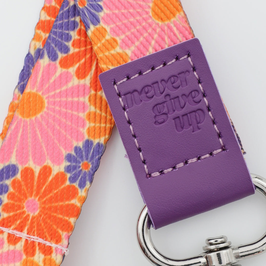 Floral strap with a purple key fob that says 'never give up' on a light gray background