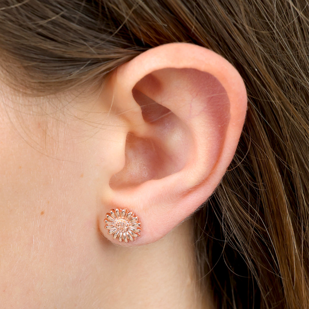 Close-up of an ear wearing a rose gold floral earring with brown hair.