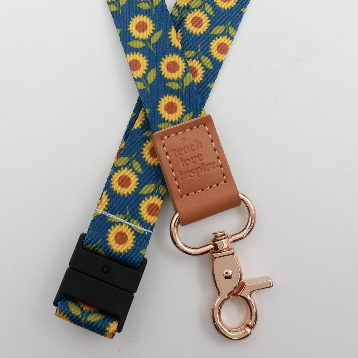 Teach Love Inspire embossed on a navy sunflower lanyard with brown trim and a lobster clasp.