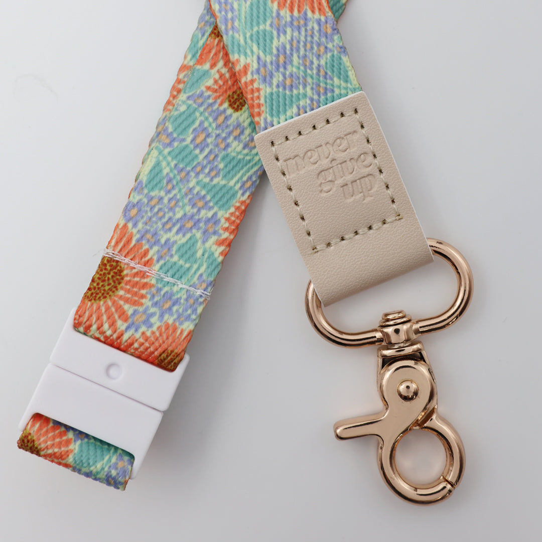 Keychain with floral strap and 'never give up' tag on a light gray background