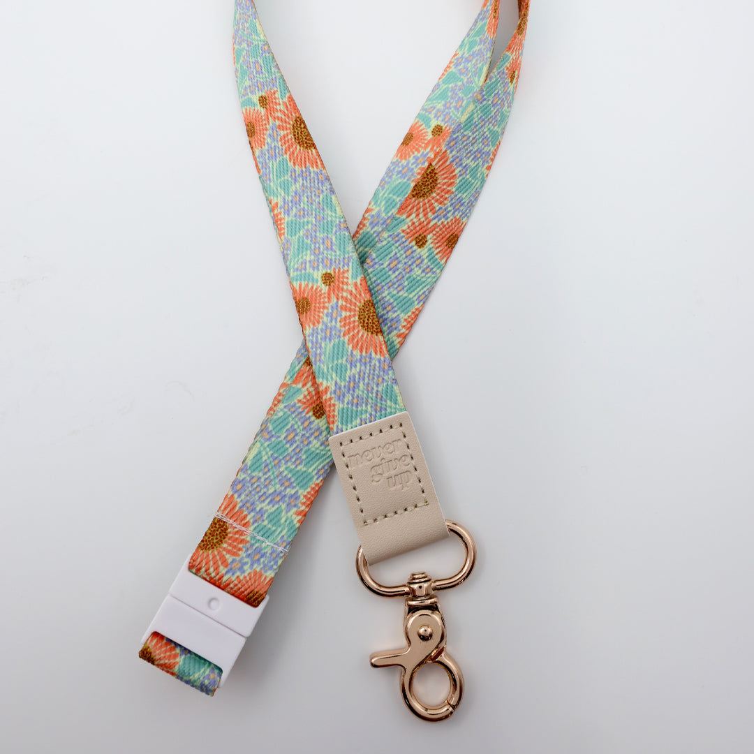 Floral patterned lanyard with a beige clip and rose gold clasp on a light gray background