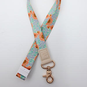 Floral patterned lanyard with a beige clip and rose gold clasp on a light gray background